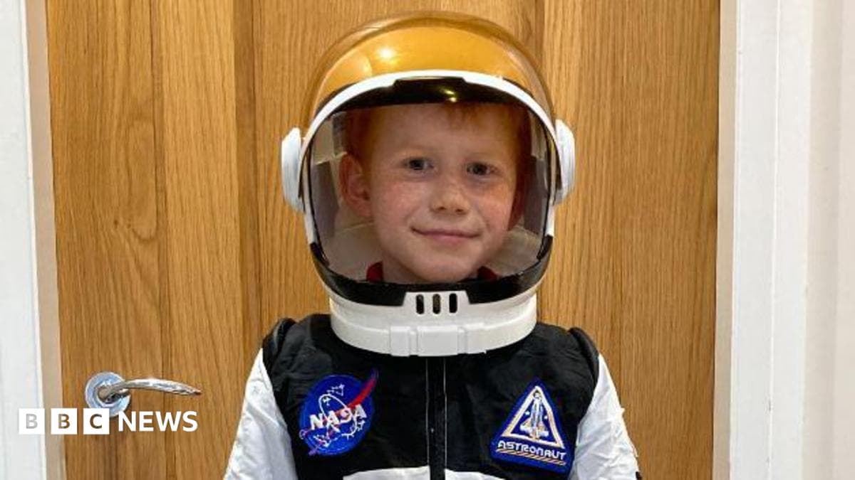 Efan in a white spacesuit and helmet. He is smiling at the camera.