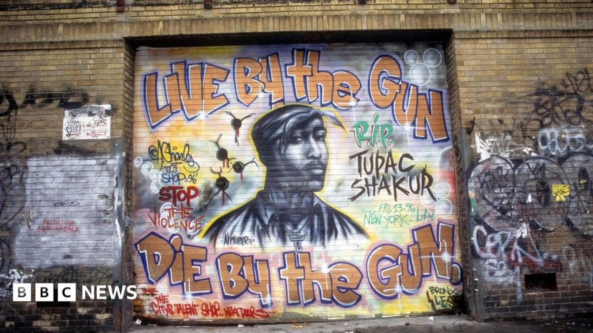 A mural of Tupac shows his face, and the phrase: Live by the gun die by the gun