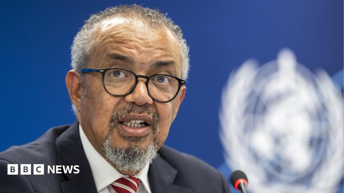 A man with grey curly hair, a beard and black glasses speaks into a microphone.