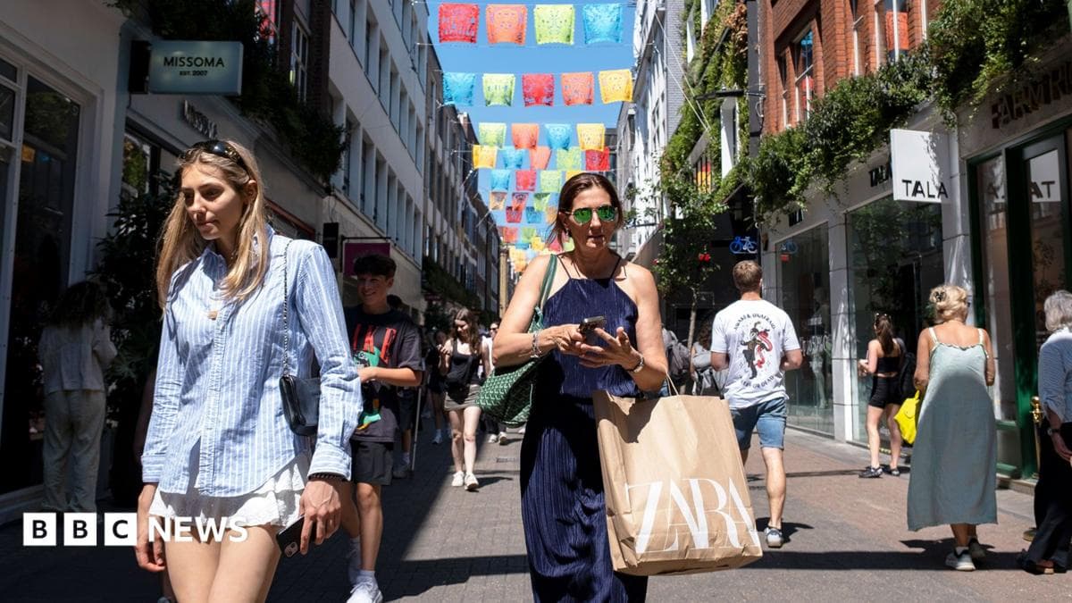 two shoppers on a busy shopping street in London walking towards the camera wearing summery clothing