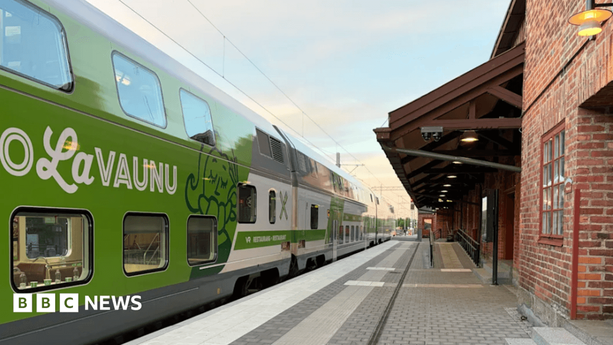 A green and white double-decker Finnish VR train pulls into a railway station.