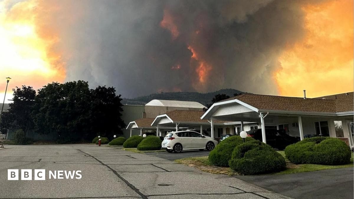 An image showing grey and orange smoke rising from behind a row of homes on a residential street in Summerland, British Columbia.