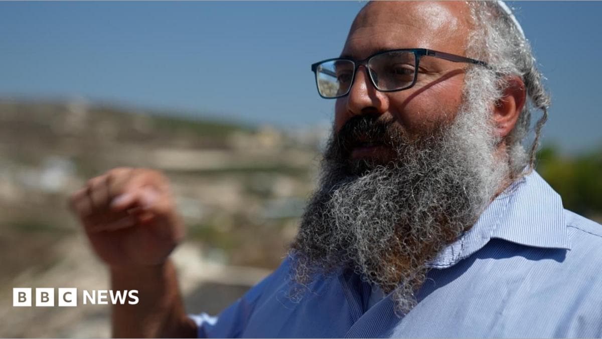 Yehuda Shimon, a large, bearded man wearing glasses, gestures with his hand