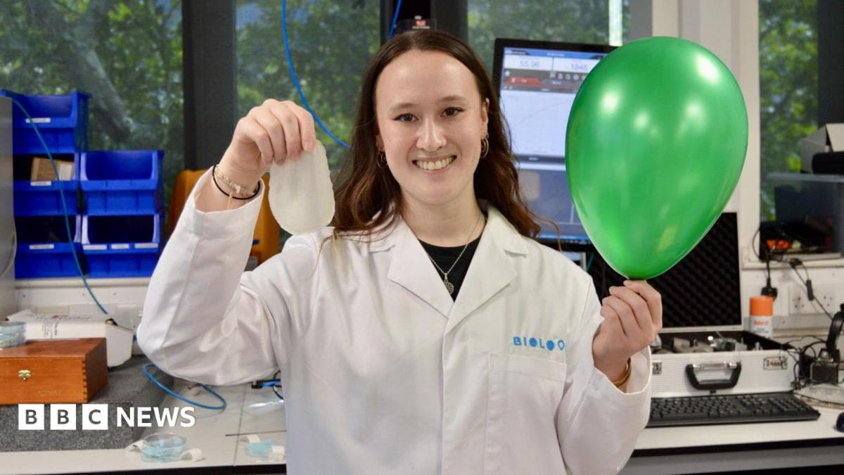 A woman in a lab coat who is holding a green balloon looks at the camera
