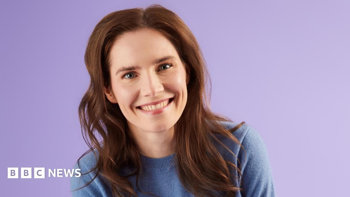 Amanda Knox. A 39-year-old woman with long brown hair and wearing a blue jumper smiles at the camera. She is in front of a plain purple background.