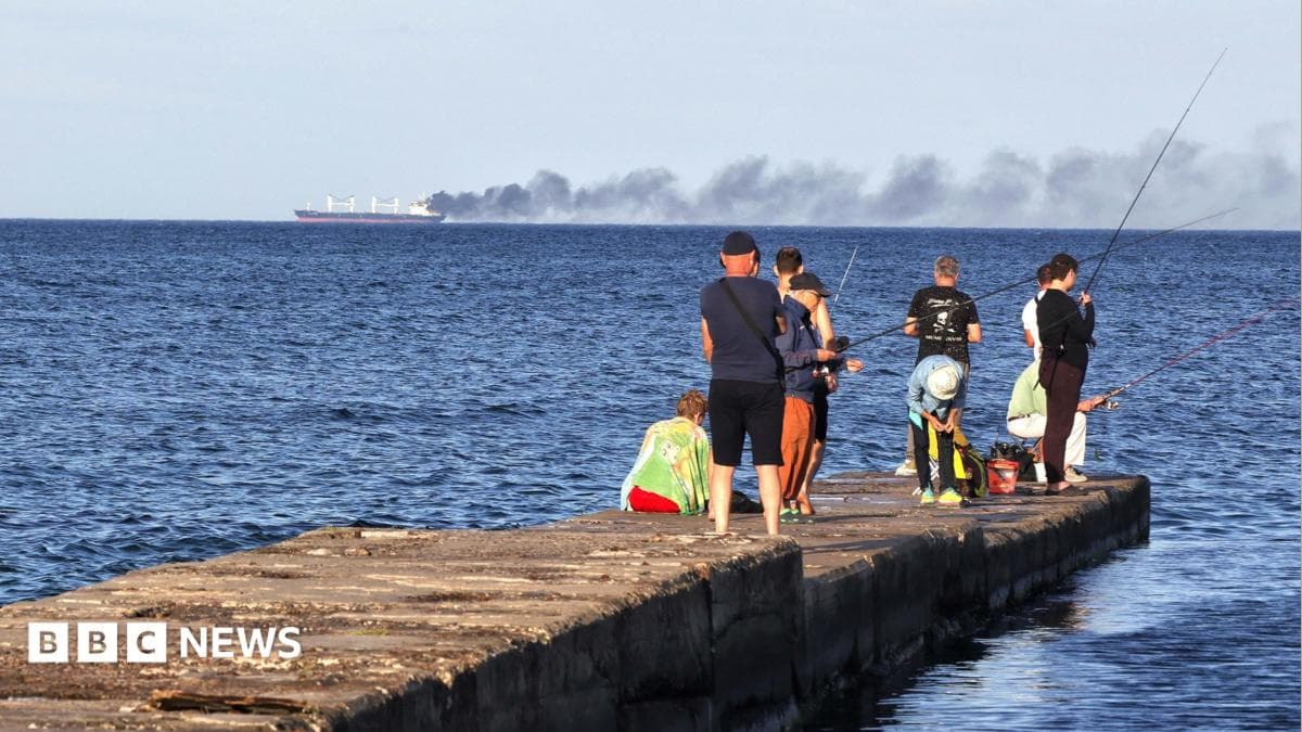 Men fish on a pier as black smoke rises from a vessel damaged by a Russian attack in the Black Sea, Odesa region, Ukraine, July 28, 2026