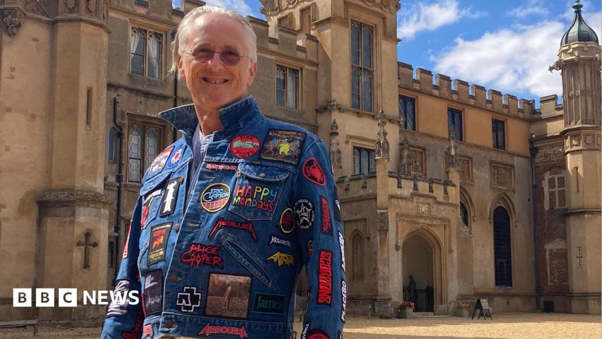 A man with grey hair is stood outside Knebworth house wearing a blue denim jacket covered in band badges