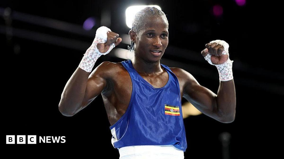 Nuhu Batte, a boxer wearing a blue top with a small Ugandan flag printed on it, holds his fists up in the air while standing in a boxing ring.