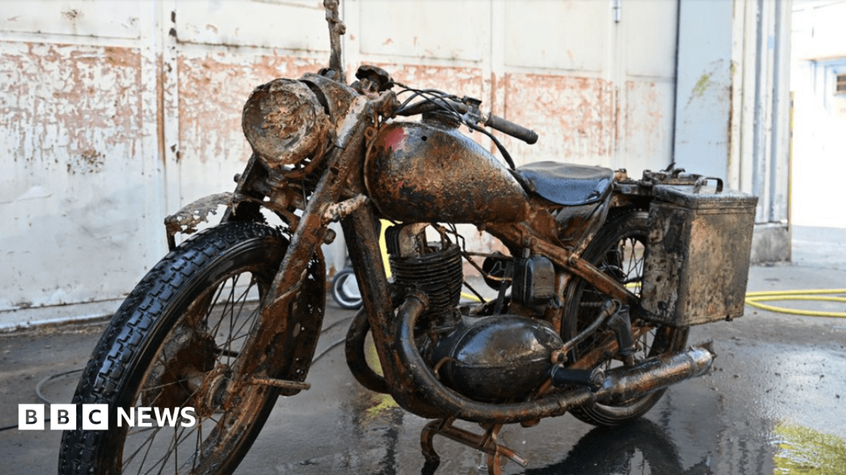 A rusted but largely well-preserved World War Two-era Wehrmacht motorcycle pictured parked in a building resembling a warehouse.