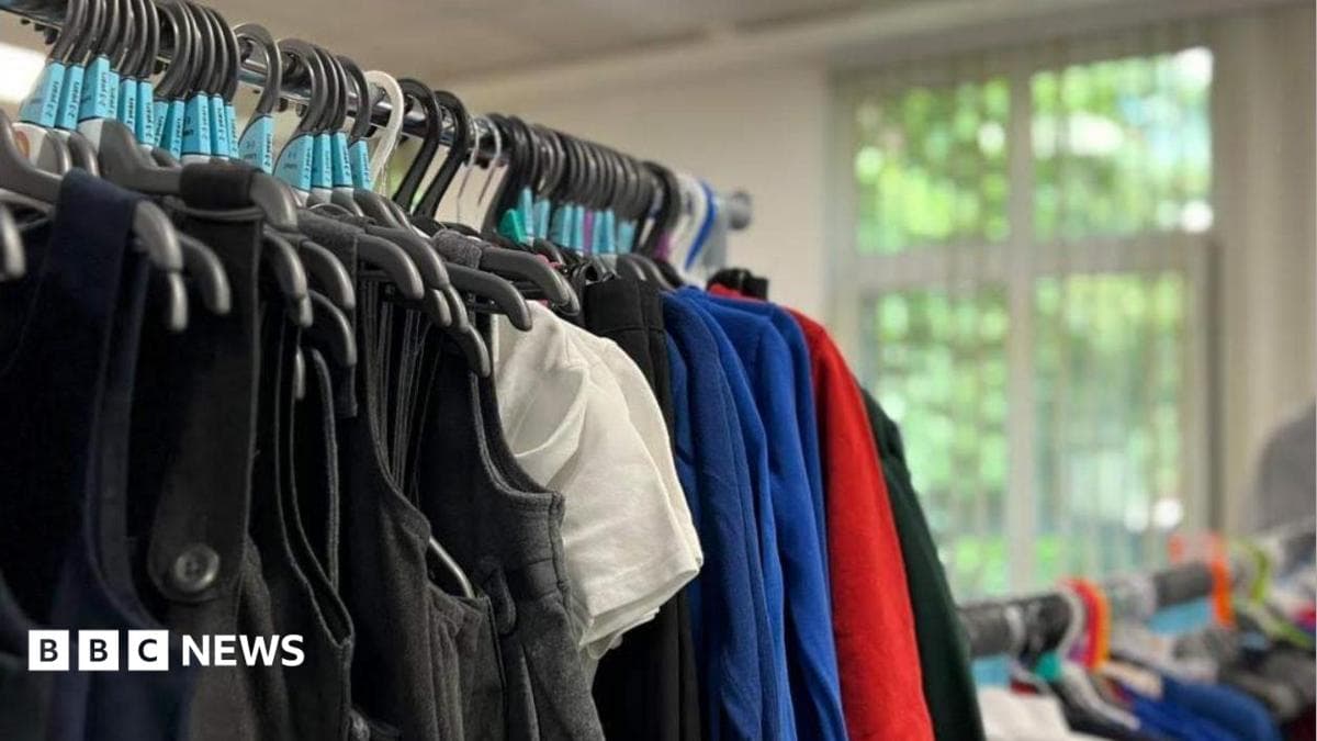 A rail of uniforms with white shirts, blue jumpers, grey pinafores and red sweatshirts on hangers.