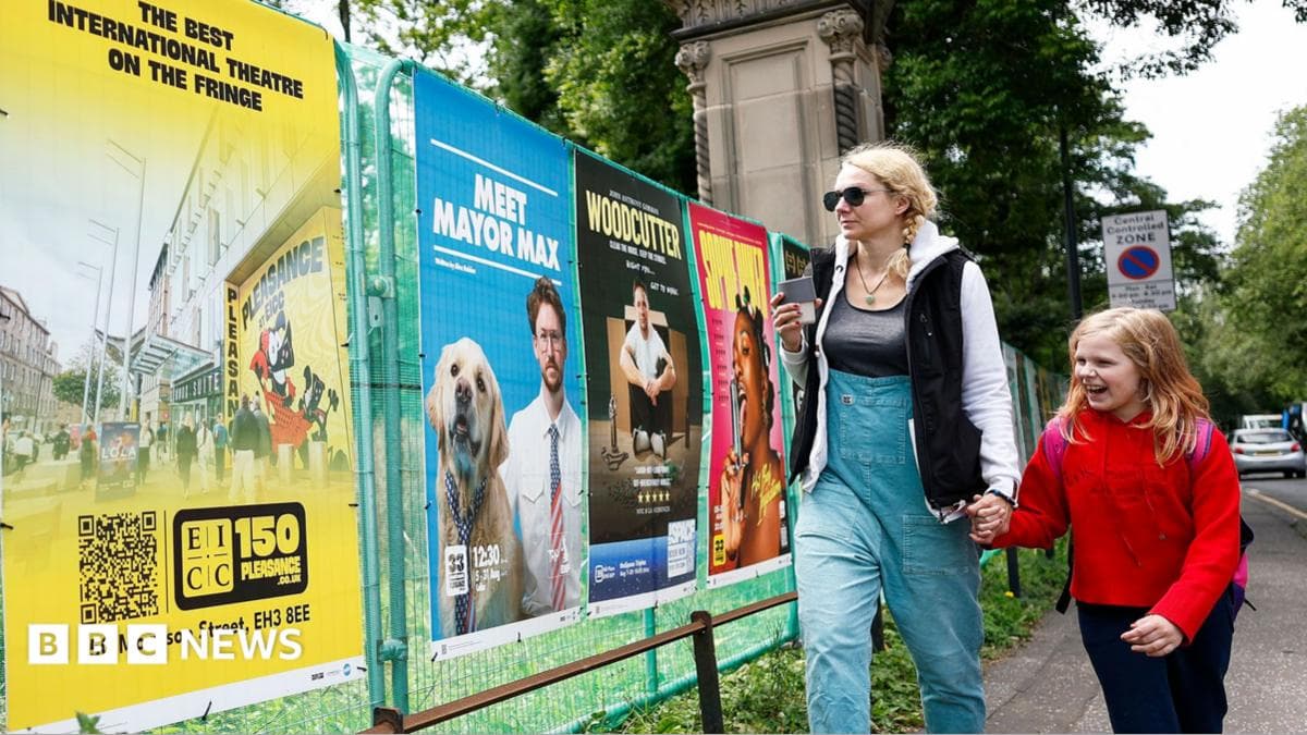 A woman and child walk past colourful posters for the Edinburgh Fringe festival on a street in Edinburgh