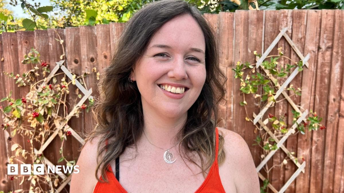 A white woman with brown hair and an orange top smiles at the camera