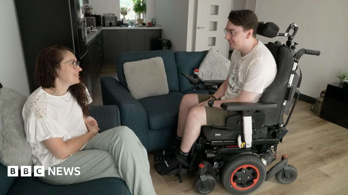 Jack in electric wheelchair next to his mother who is sitting on sofa in their living room