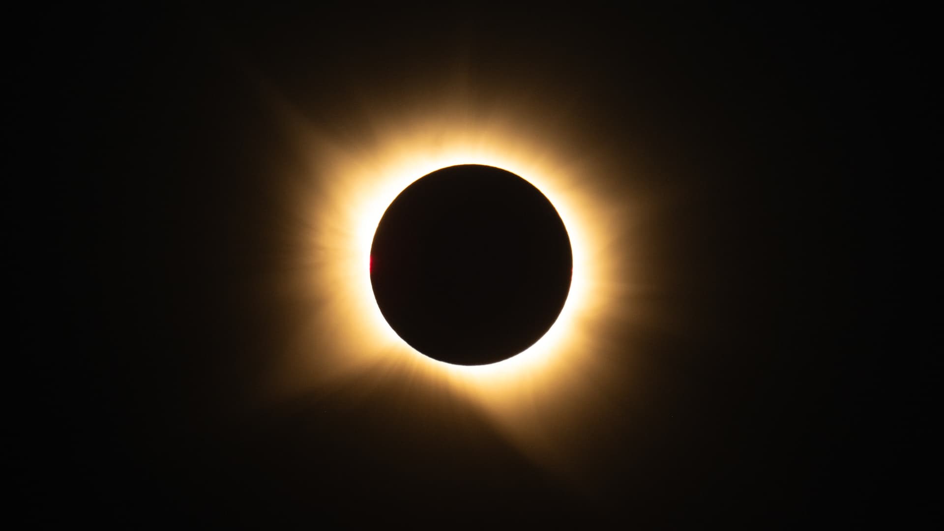 The light of the Sun makes a fiery yellow halo around the Moon during a total solar eclipse. There is a hint of red at the 9 o'clock position on the Moon's edge.